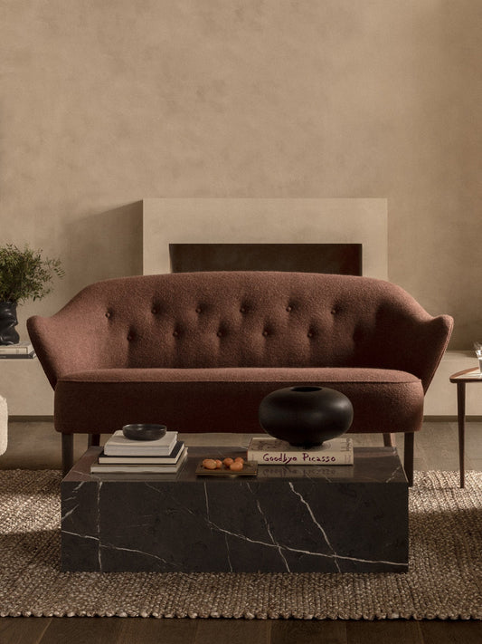 The Ingeborg Sofa in brown fabric shown in a living room with a black marble Plinth Low coffee table in front of a fireplace.