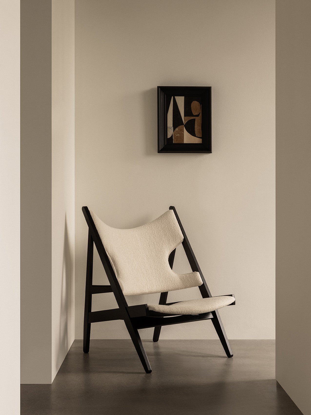 The Knitting Lounge Chair in black oak with ivory bouclé upholstery, in a corner beneath a framed abstract painting.