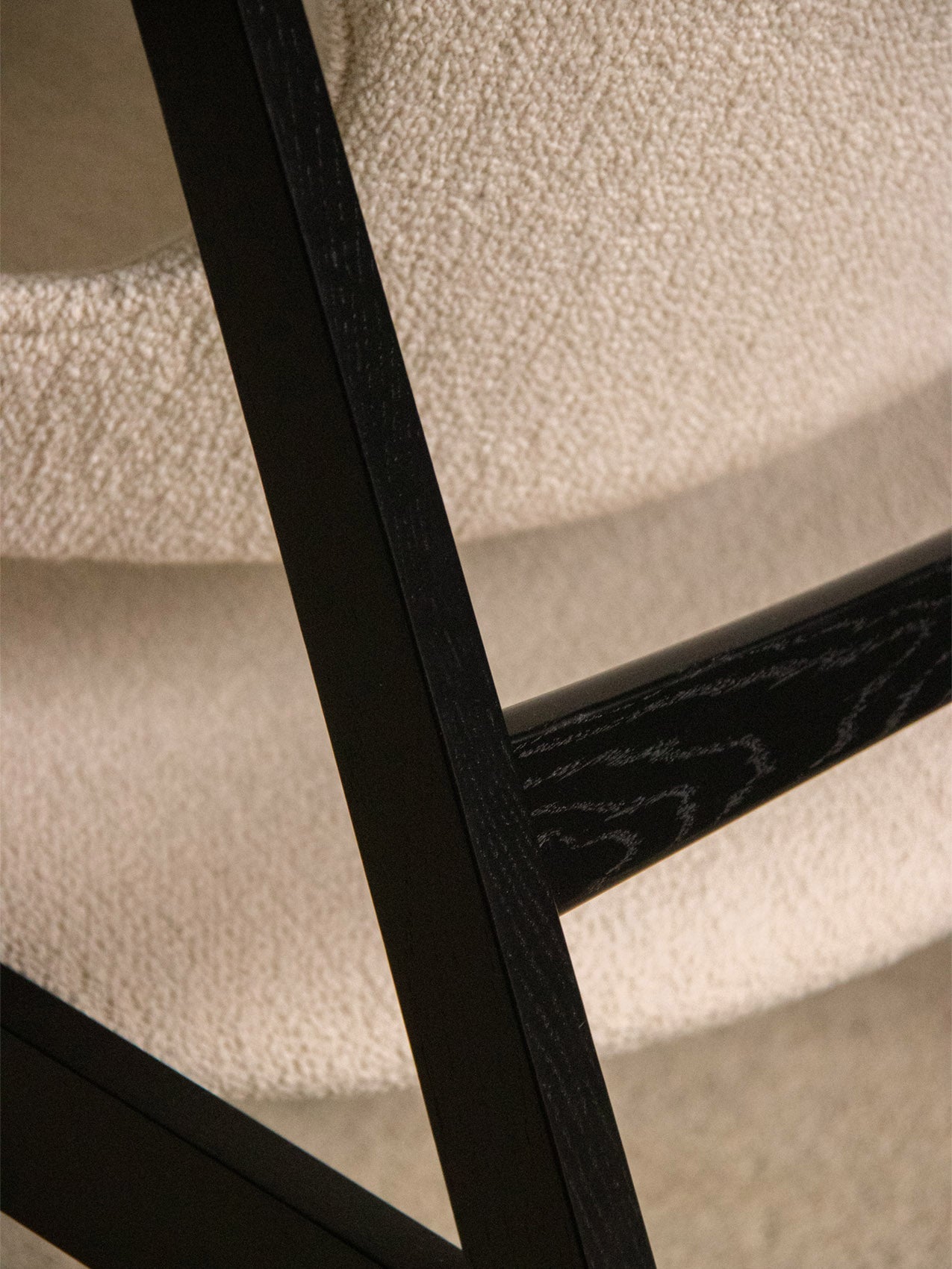 Close-up showing the textural contrast of the Knitting Lounge Chair's ivory bouclé seat and black oak frame.
