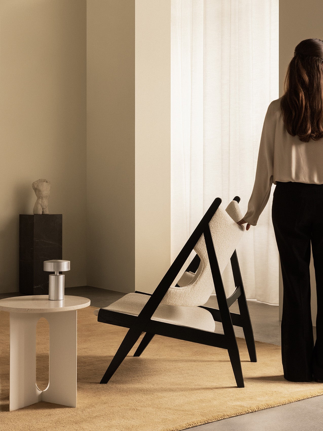 The black oak Knitting Lounge Chair styled in a room with an Androgyne Side Table, Column Table Lamp, and Plinth Pedestal.