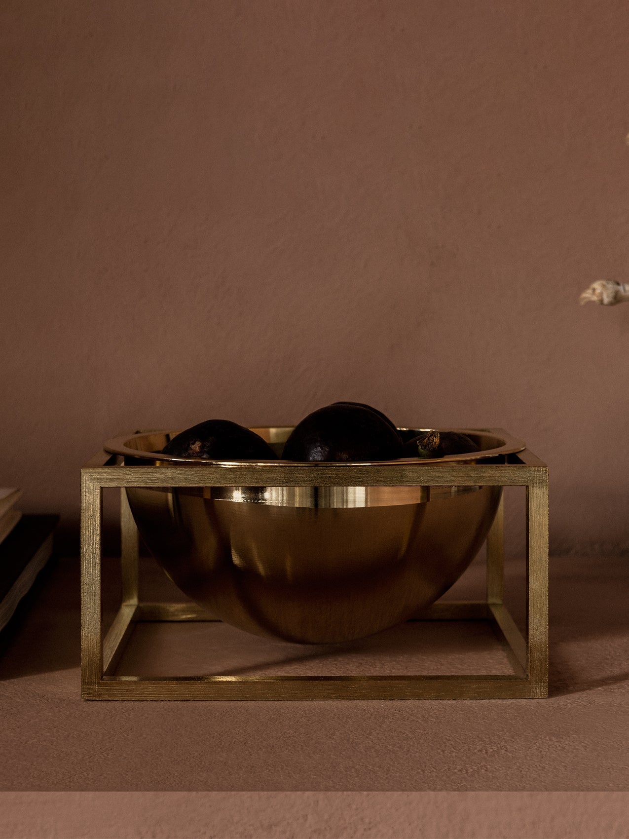 Close-up of the brass Audo Kubus Centrepiece. The bowl, held in a square frame, is filled with dark figs on a brown surface.