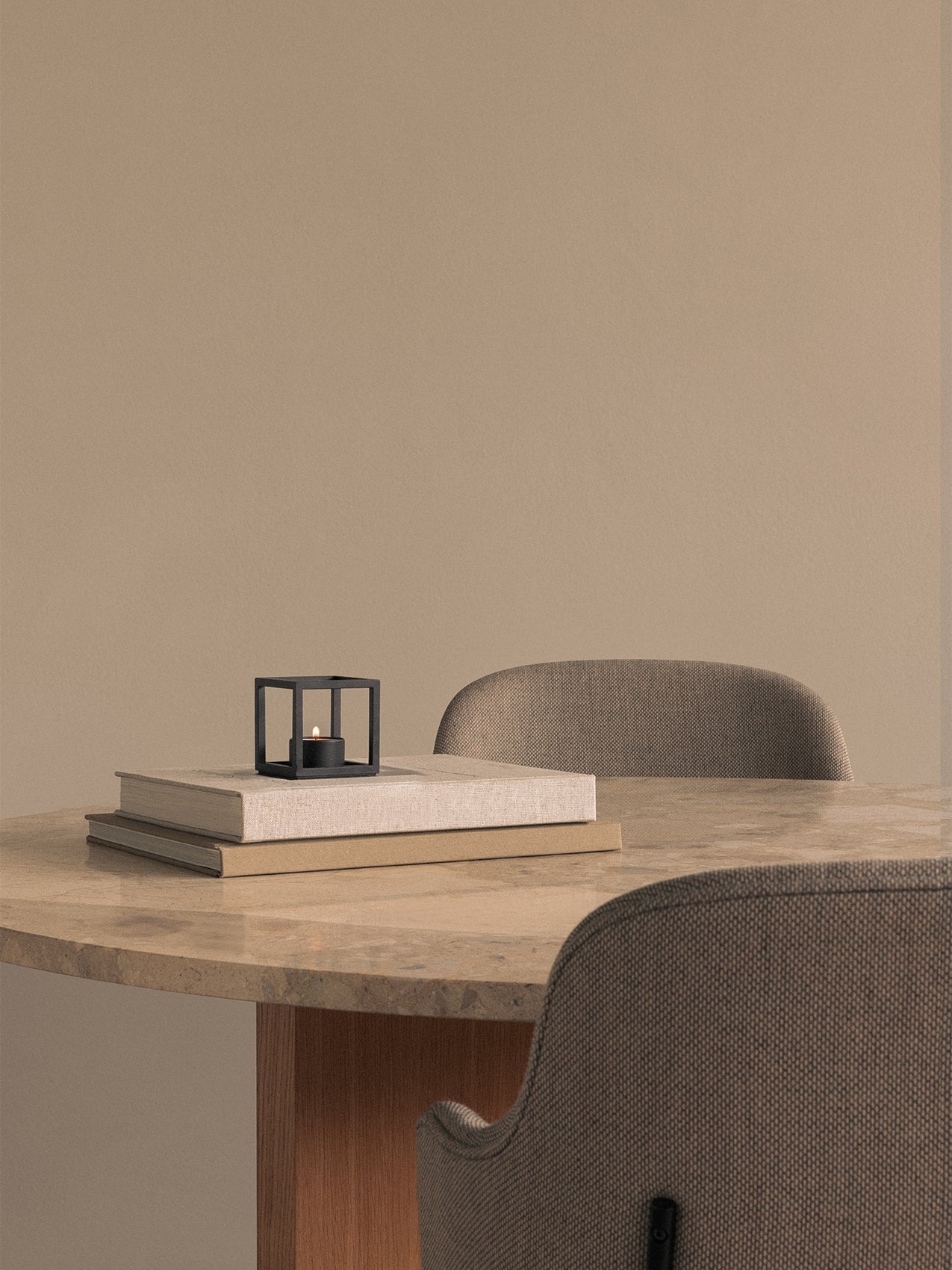 A black Kubus T tealight holder with lit candle on books on a marble Androgyne Dining Table, with Penguin Dining Chairs.