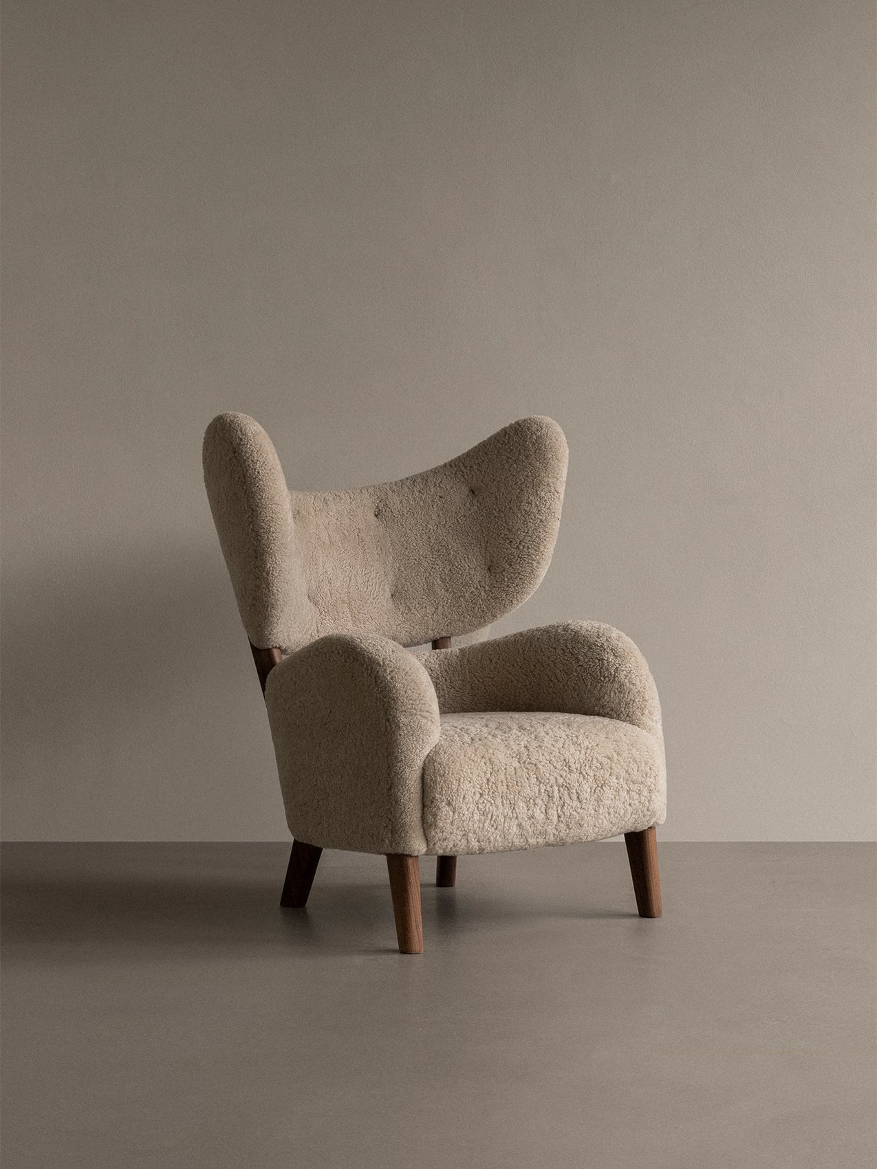 My Own Chair upholstered in Sheepskin Moonlight with a walnut frame, shown from a three-quarter angle in a minimalist room.