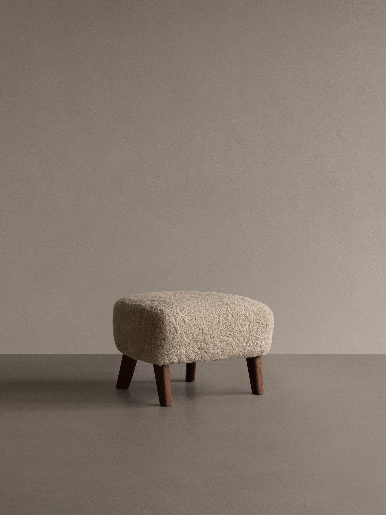 A My Own Chair, Ottoman, with a plush Sheepskin Moonlight seat and four dark wood legs, seen in a minimalist studio setting.