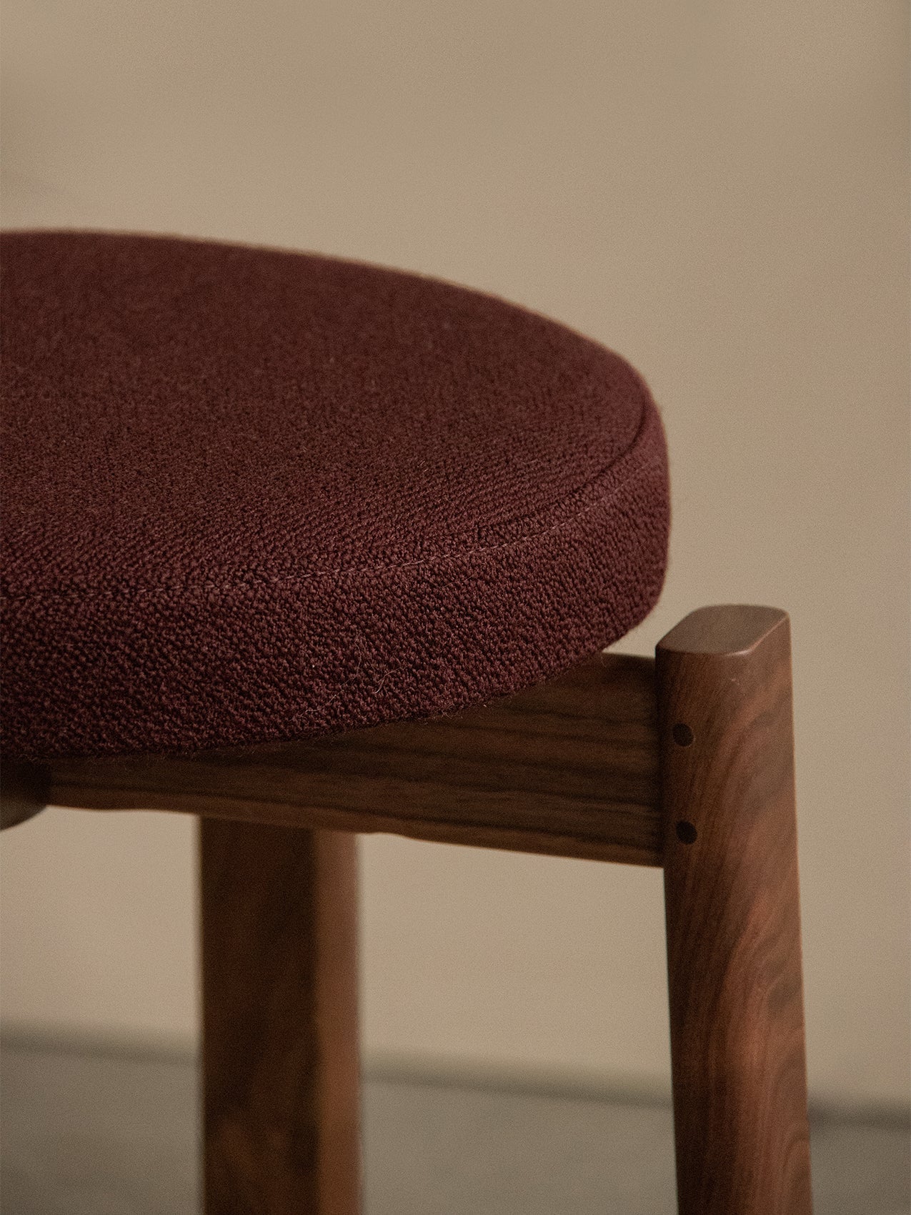 Detailed view of the Passage Stool, Upholstered, showing the joinery of its dark walnut frame and textured burgundy seat.