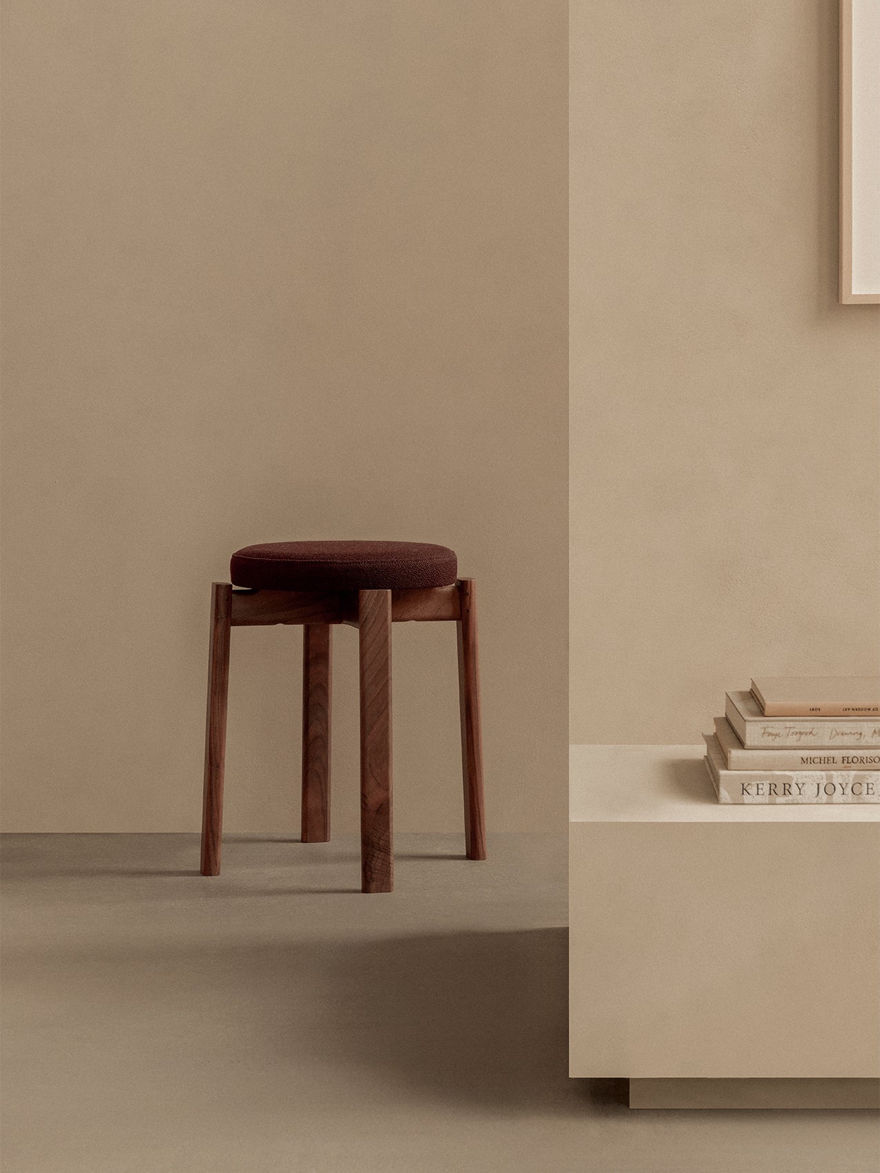 The Passage Stool, Upholstered in dark walnut with a round brown fabric seat, shown in a minimalist room with beige walls.