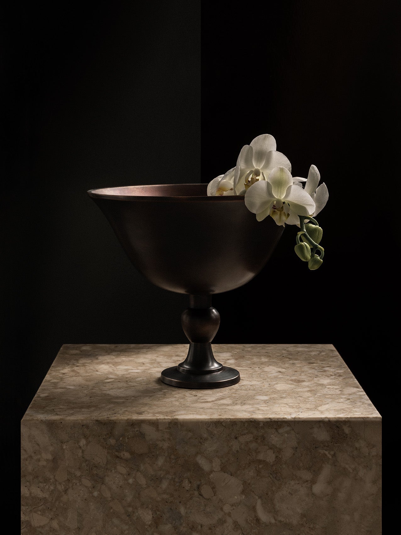 The Audo Pavot Bowl in a dark bronze finish, displayed on a marble block with a white orchid draped over its edge.