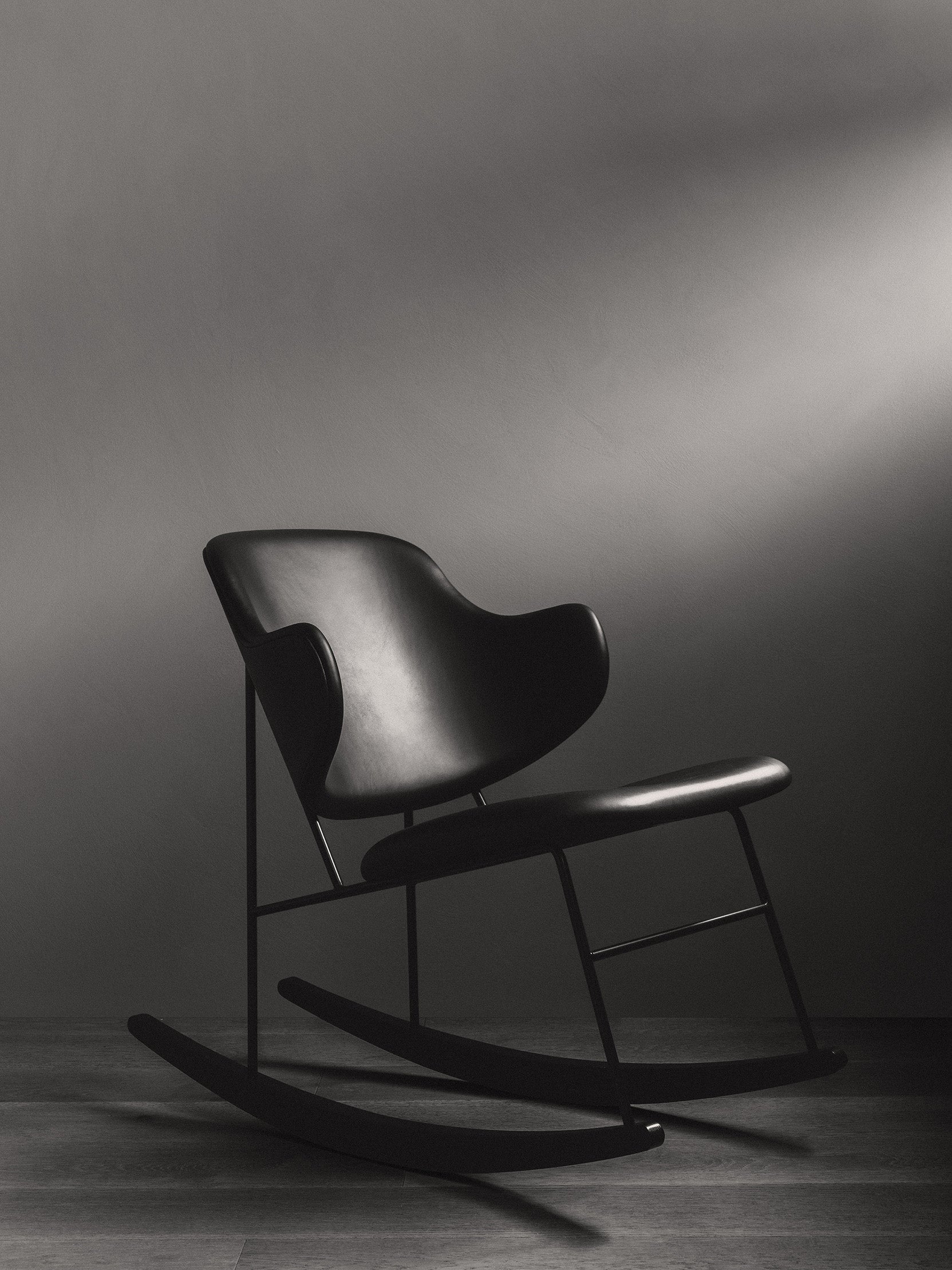 The black Penguin Rocking Chair, fully upholstered, seen from the side in a dark room with dramatic overhead lighting.