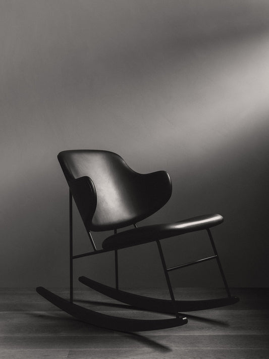 The black Penguin Rocking Chair, fully upholstered, seen from the side in a dark room with dramatic overhead lighting.