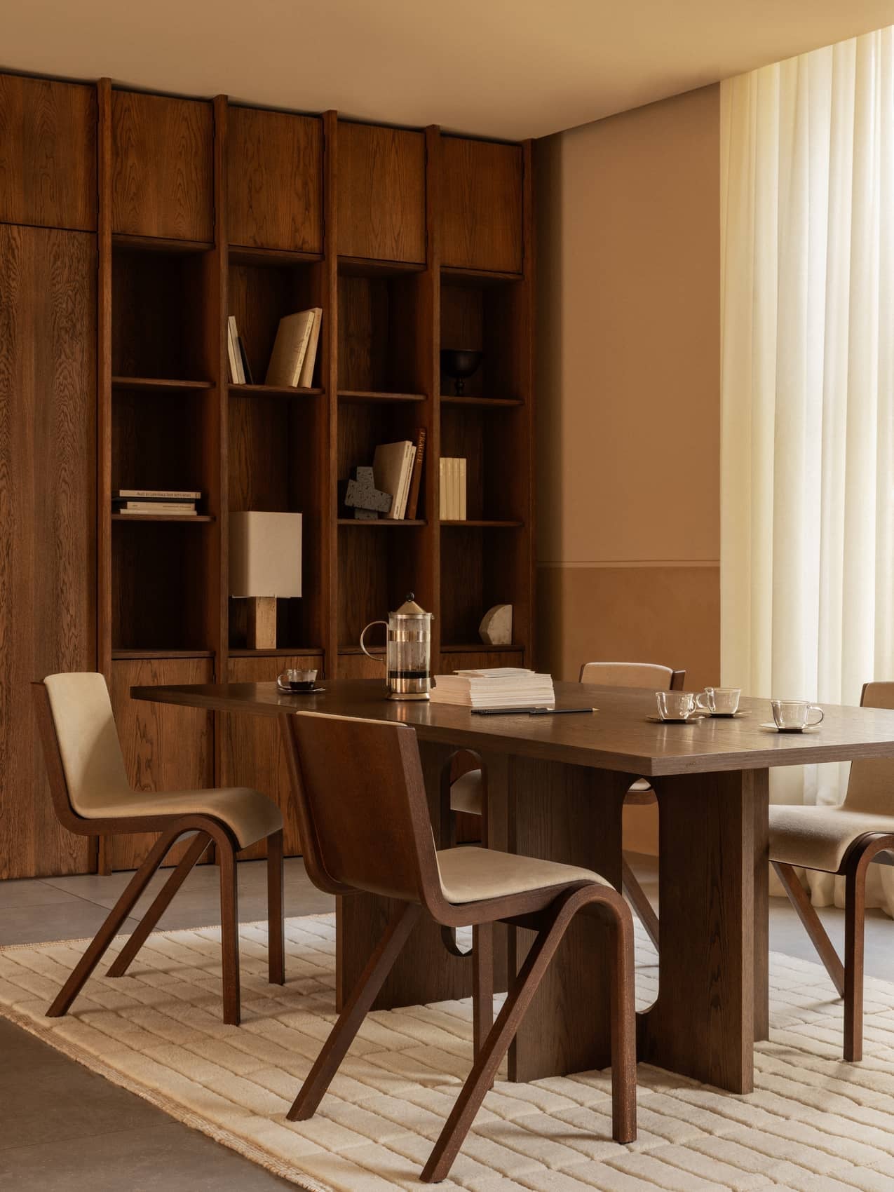 A dining room with an Androgyne Table, Ready Chairs, and Tile Rug. A bookcase holds a Nonna Lamp and Convergence Bookends.