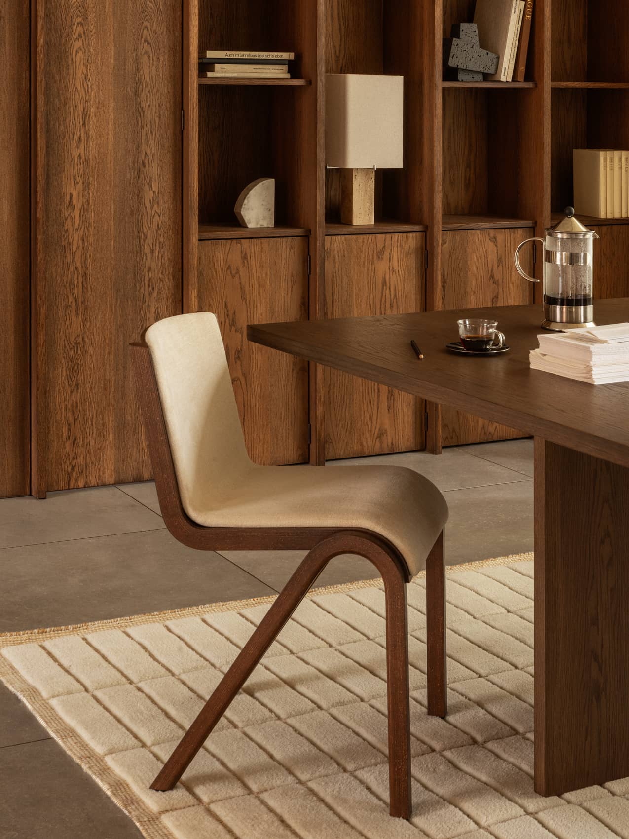 A Ready Dining Chair at an Androgyne Dining Table, with a Nonna Lamp and Convergence Bookends on shelves behind.