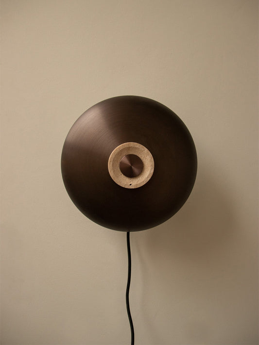 Front view of the Reverse Wall Lamp on a plain wall, highlighting its bronzed aluminium shade and central travertine dimmer.
