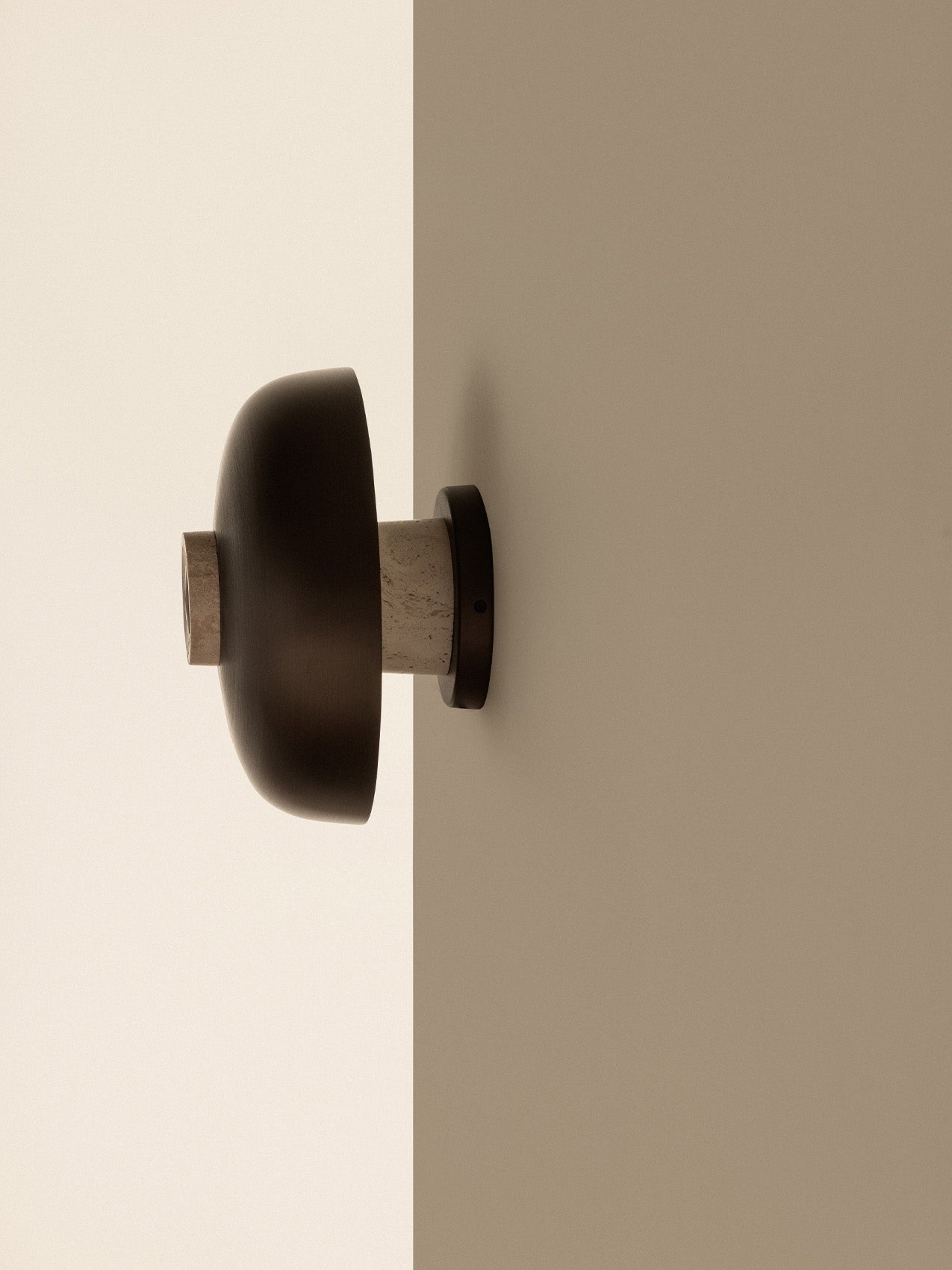 Side view of the Reverse Wall Lamp with its bronzed aluminium shade and travertine base, mounted on the corner of a wall.