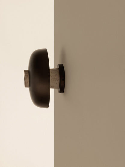 Side view of the Reverse Wall Lamp with its bronzed aluminium shade and travertine base, mounted on the corner of a wall.