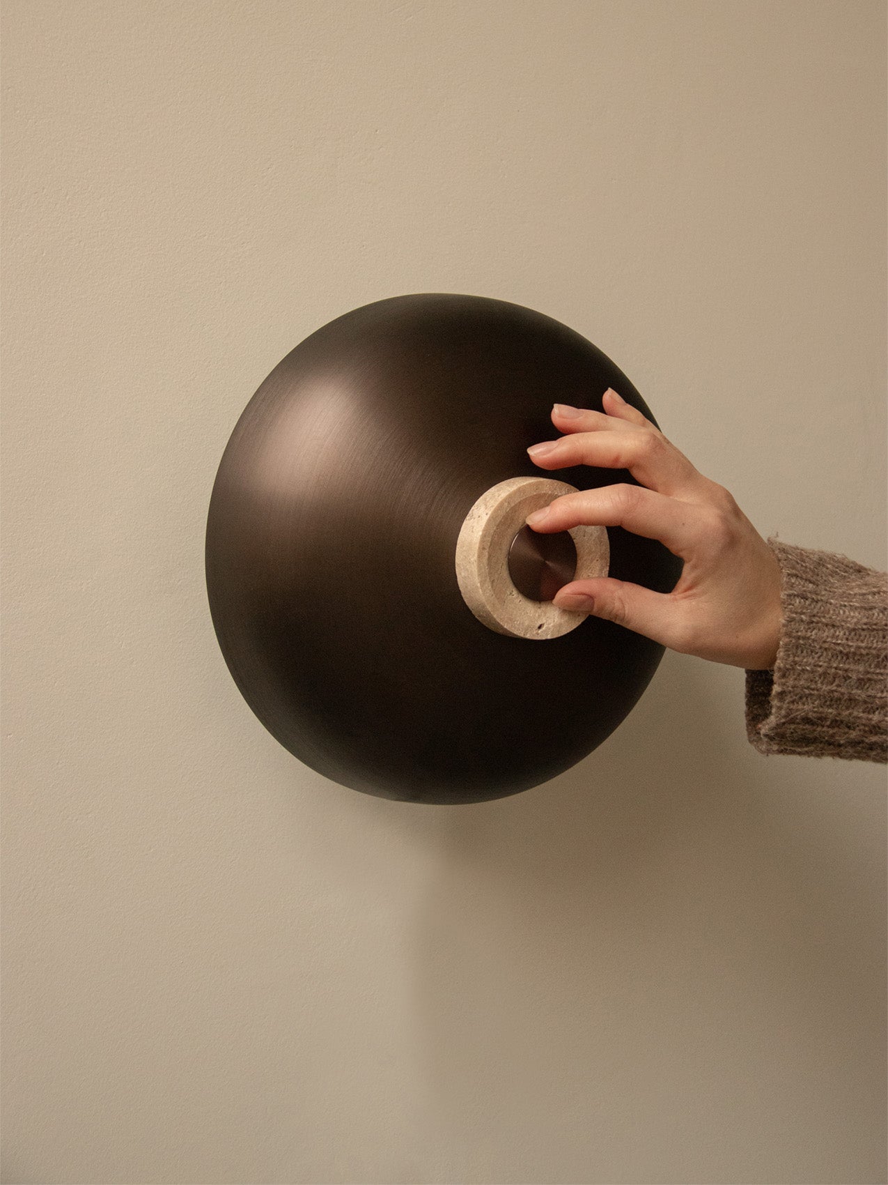 A close-up of a hand adjusting the travertine stone dimmer on the bronzed aluminium shade of the Reverse Wall Lamp.