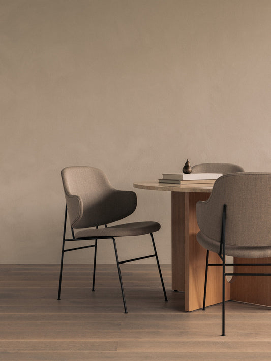 Two upholstered Penguin Dining Chairs surround an Androgyne Dining Table with books and a Sentiment Paper Weight on top.
