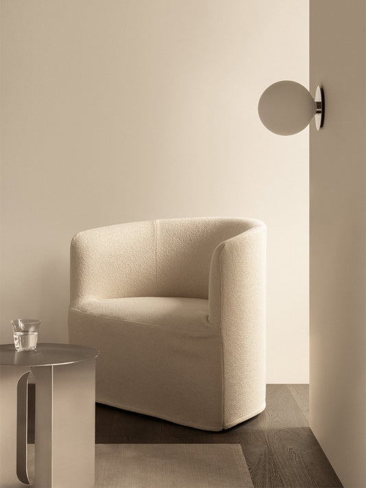 A cream Tearoom Lounge Chair with Loose Cover next to an Androgyne Side Table in a neutral room with a TR Bulb Wall Lamp.