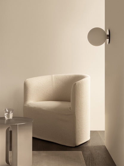 A serene setting with a cream Tearoom Lounge Chair, a grey Androgyne Side Table, and a TR Bulb Wall Lamp on the wall.