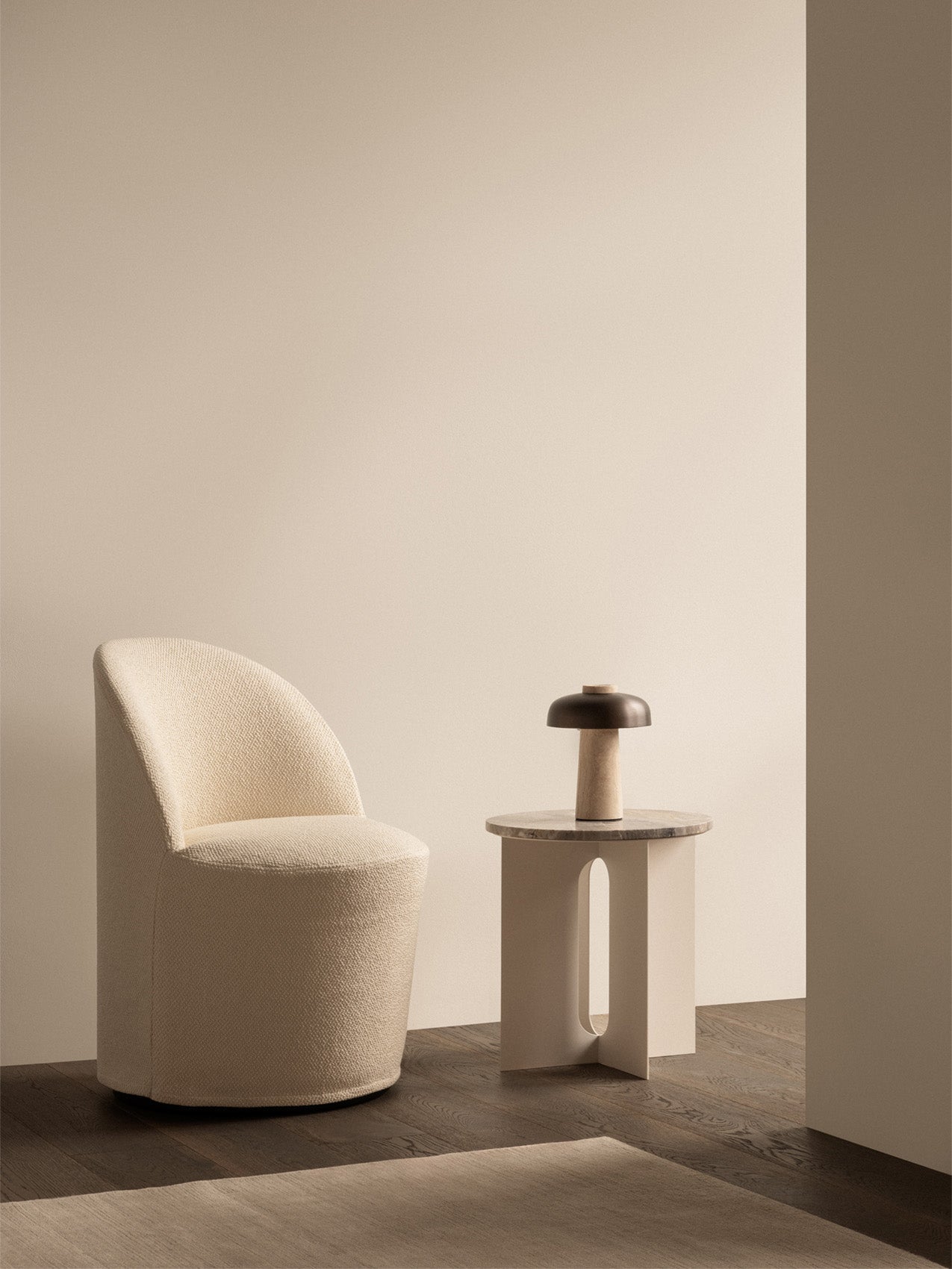 A cream Tearoom Club Chair with swivel base, next to an Androgyne Side Table and Reverse Table Lamp in a minimalist setting.
