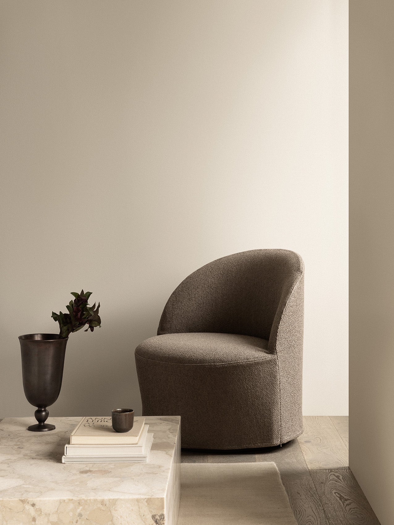 The Tearoom Lounge Chair Swivel in textured brown fabric beside a Plinth Low marble table with a Pavot Vase with foliage.