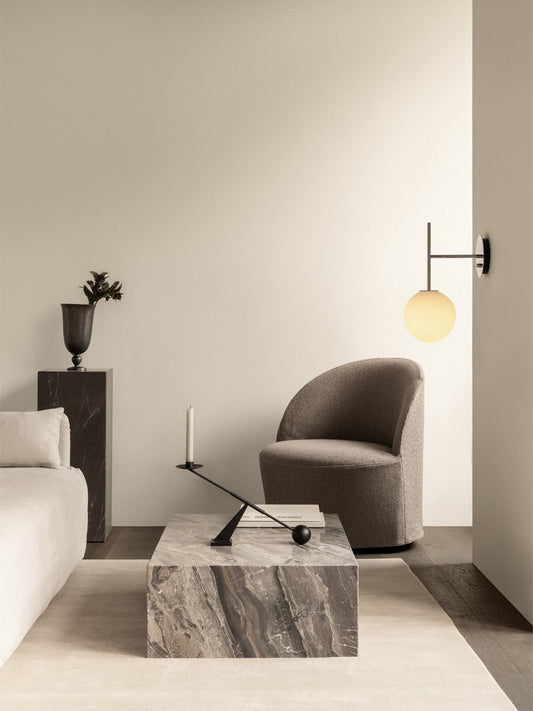 A grey Tearoom Lounge Chair sits by a Plinth Low marble table. A TR Bulb wall lamp glows above, in a modern living room.