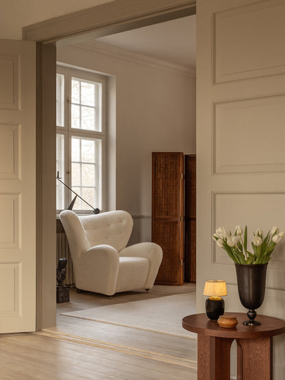 A white Tired Man Lounge Chair by a window. An Androgyne Side Table holds a Torso lamp and a Pavot Vase in the foreground.