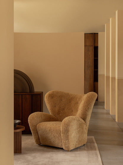 The Tired Man Lounge Chair in honey sheepskin sits on a Duomo Rug in a modern room with beige walls and dark wood furniture.