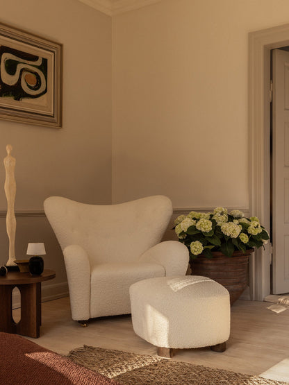 The Tired Man Lounge Chair & Ottoman in white bouclé, styled with an Androgyne Side Table, Torso Table Lamp & a potted plant.