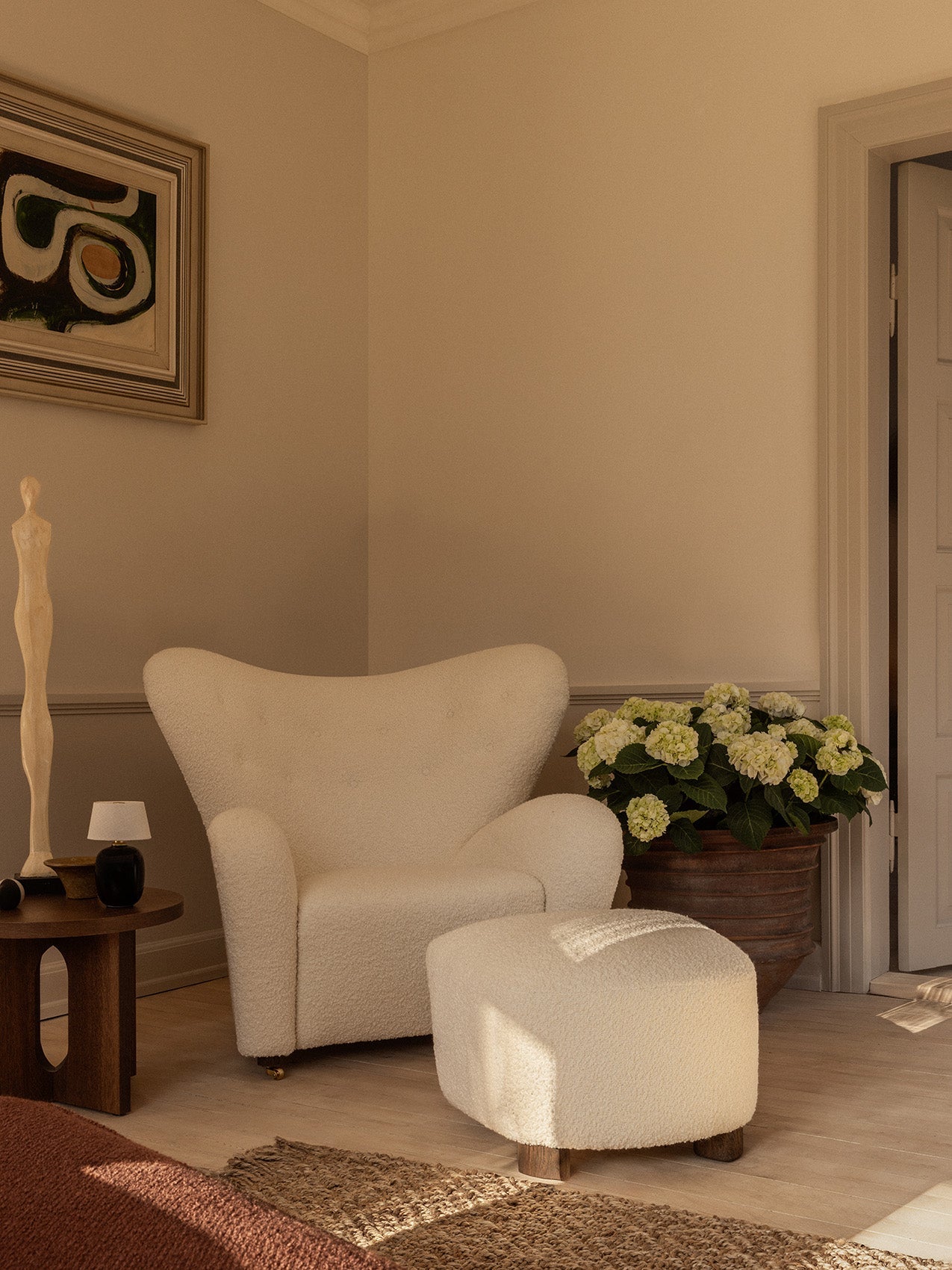 The Tired Man Lounge Chair & Ottoman in white bouclé, styled with an Androgyne Side Table, Torso Table Lamp & a potted plant.