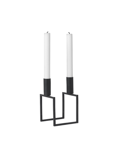 A black, geometric Kubus Line candle holder with two tall white candles, viewed from an angle against a black background.