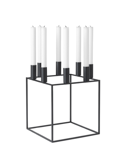 The Kubus 8 candle holder in black, a minimalist, cube-shaped metal frame holding eight tall white candles.