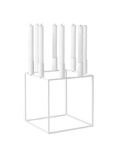 A white Kubus 8 candle holder with a minimalist cube frame, holding eight tall white candles on a black background.