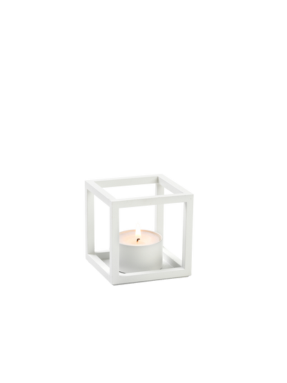 The white Kubus T tealight holder, a minimalist cube-shaped frame, shown at an angle with a lit white candle inside.