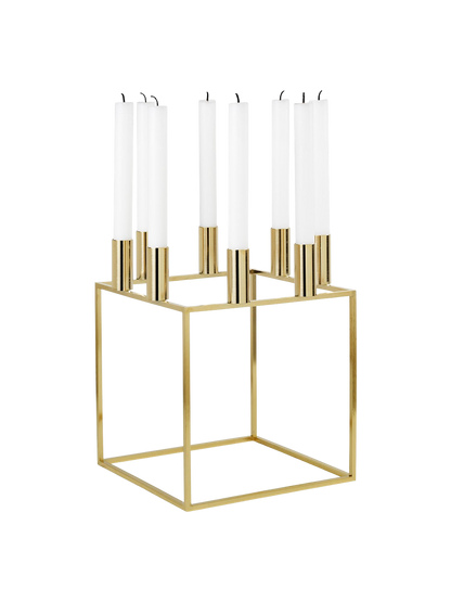 A gold-plated Kubus 8 candle holder with a square frame, holding eight unlit white candles, shown from an angle.