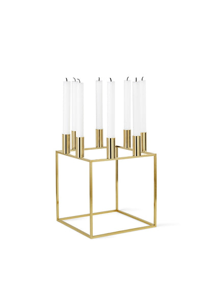 A gold-plated Kubus 8 candle holder with a geometric square base, holding eight tall, white taper candles.
