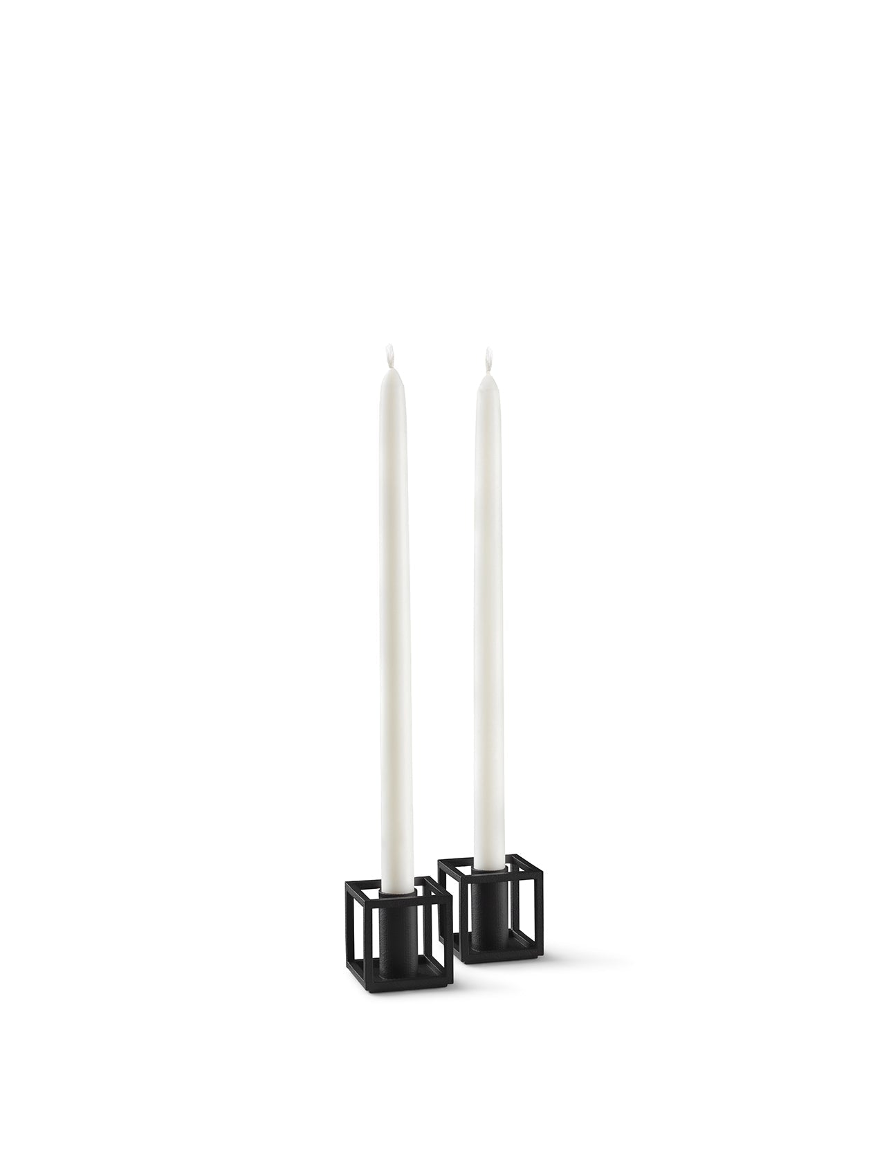 A pair of black, geometric Kubus Micro candlestick holders, each holding a tall white candle against a white background.