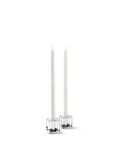 A pair of Kubus Micro candleholders in a polished nickel finish, each holding a tall, slender white taper candle.