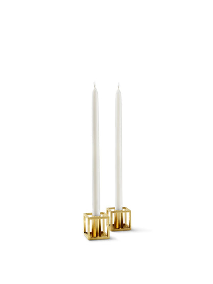 A pair of gold-plated Kubus Micro candle holders, each holding a tall, slender white candle against a plain white background.