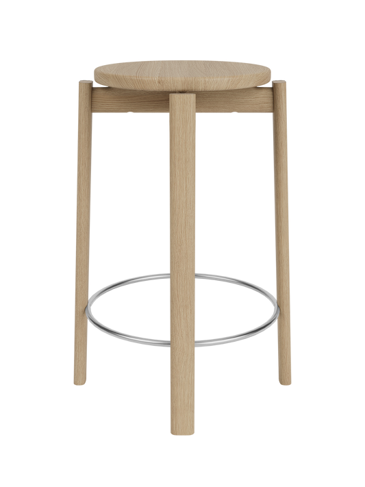 A front view of the Passage Counter Stool in natural oak, showing its round seat, three legs, and stainless steel footrest.