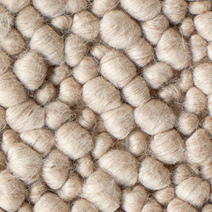 A detailed close-up of the Gravel Rug in Ivory, showcasing its bumpy, pebble-like texture of handwoven wool loops.