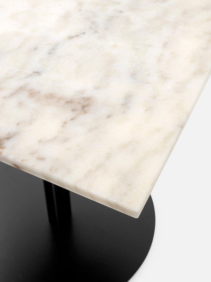 A close-up view of the corner of a Harbour Column Table, showing the off-white marble tabletop and black column base.