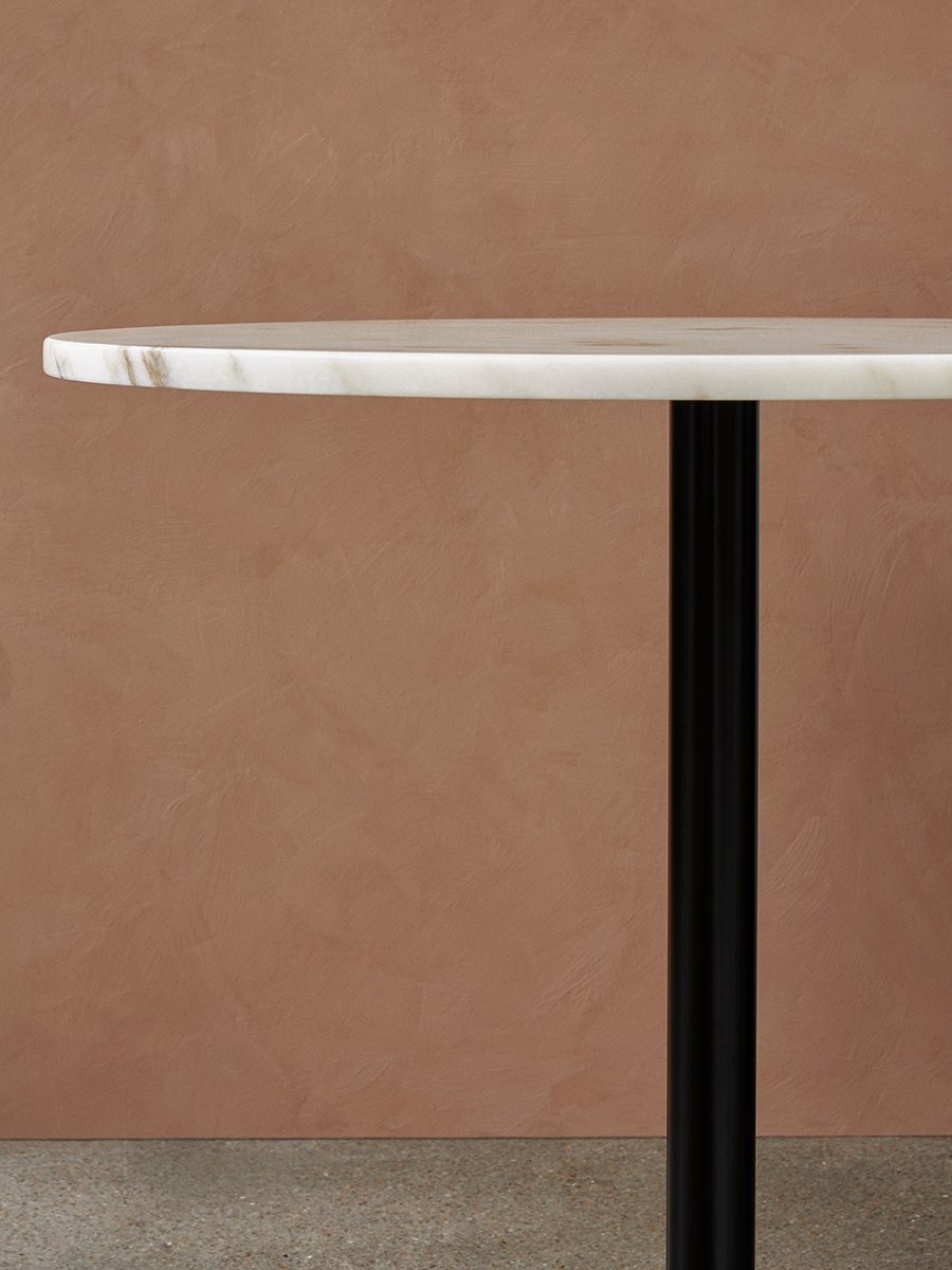 A close-up of the Harbour Column Dining Table with a white marble top and a black column base, set against a terracotta wall.