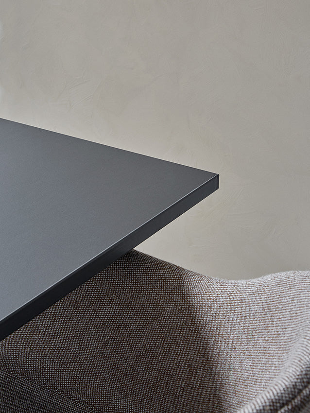 A close-up view showing the corner of the charcoal Harbour Column Table and the textured upholstery of a Harbour Chair.