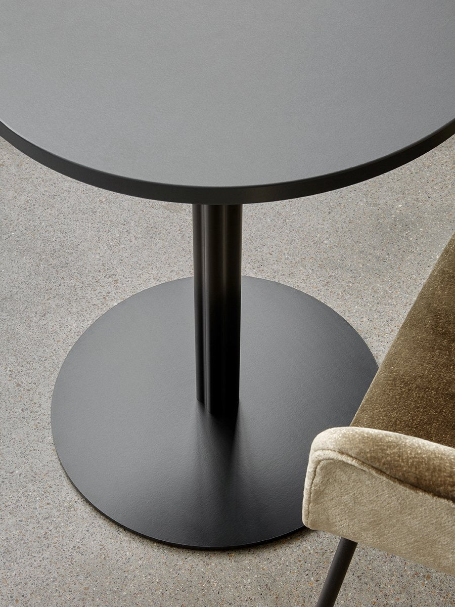 A high-angle close-up of the black Harbour Column Dining Table and olive velvet Harbour Chair on a grey concrete floor.