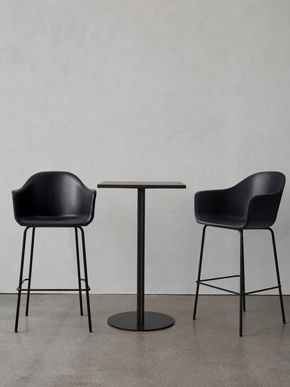 A black Harbour Column Bar Table with a rectangular top and round base, flanked by two black upholstered Harbour Bar Chairs.