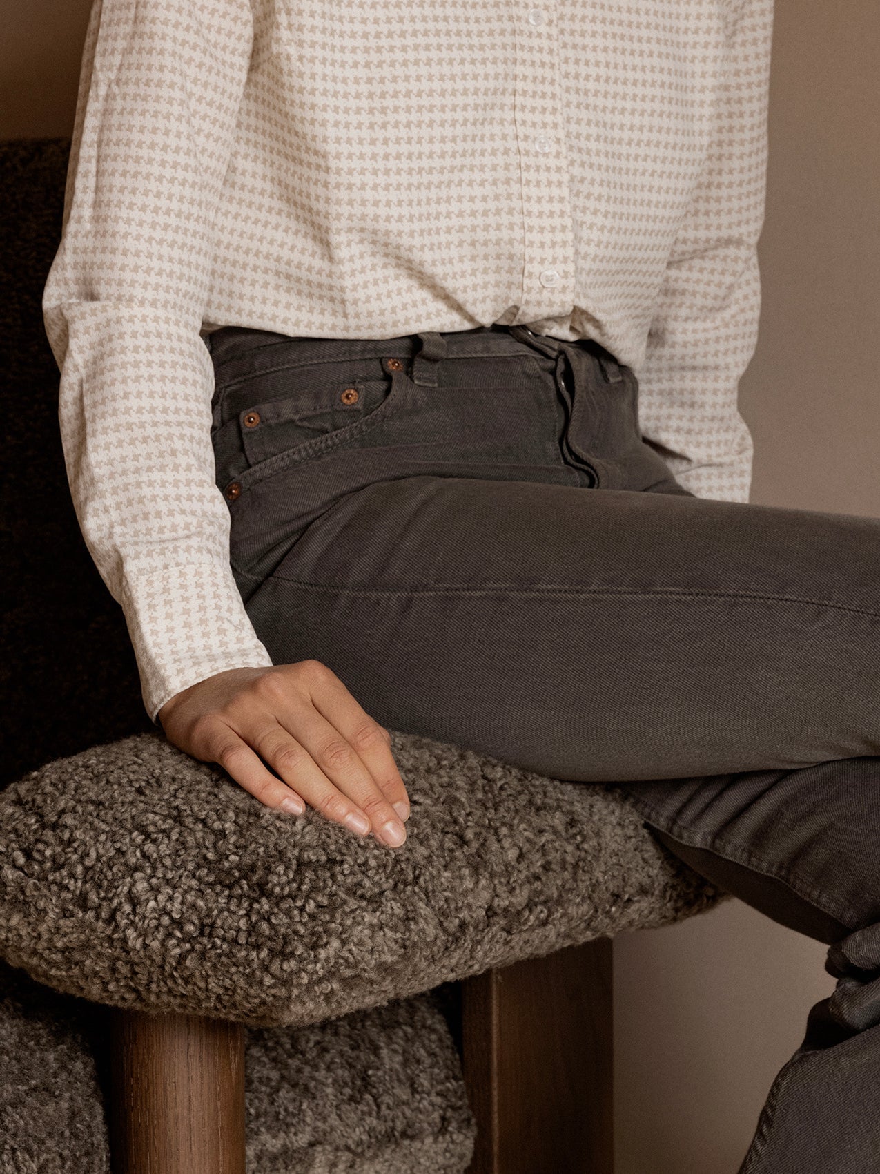 A person in a patterned shirt and jeans sits in the Brasilia Lounge Chair, hand resting on the plush, dark sheepskin armrest.
