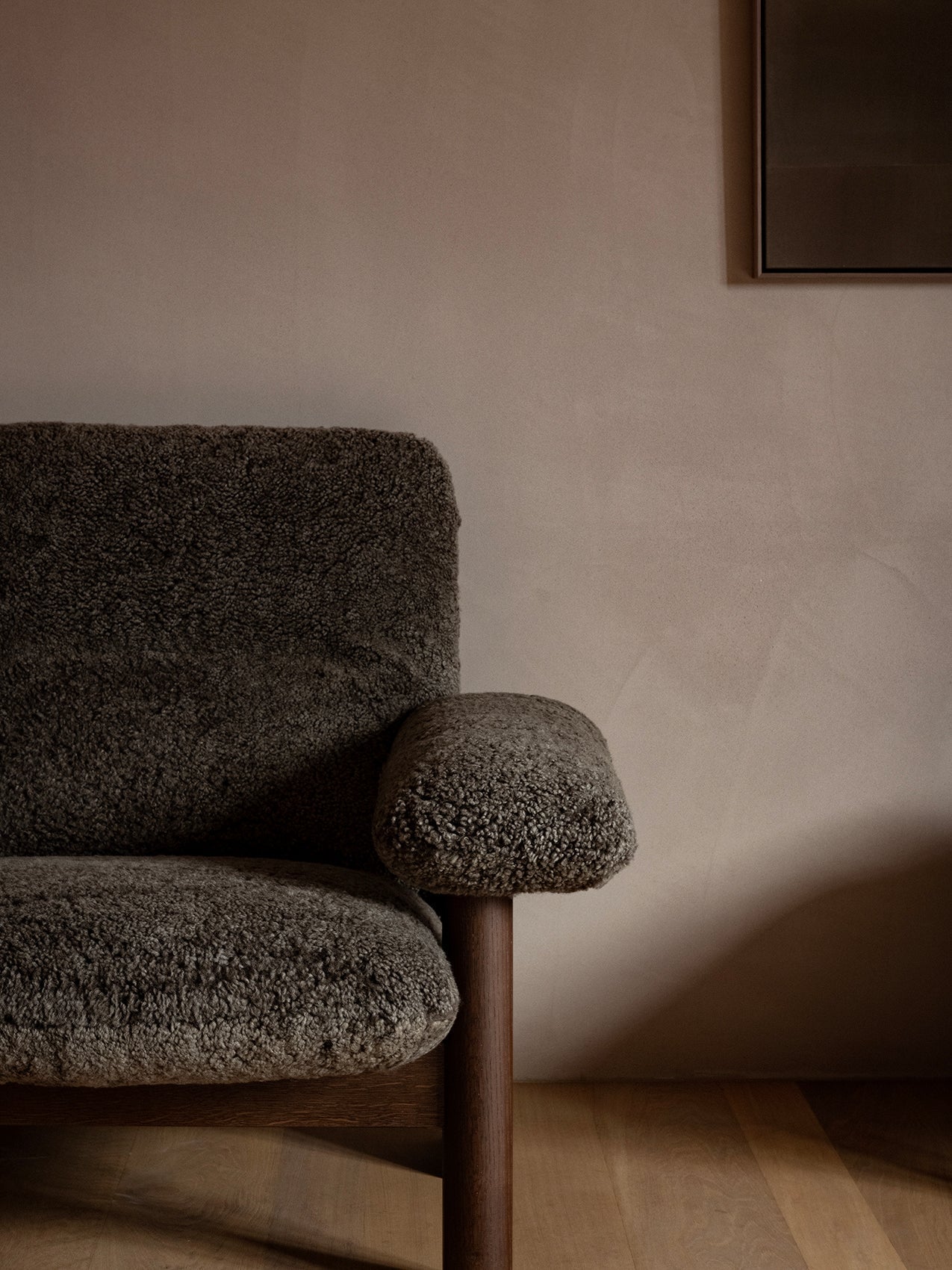 Close-up of the Brasilia Lounge Chair in dark sheepskin, showing the exaggerated armrest and dark wood leg.