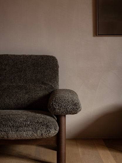 Close-up of the Brasilia Lounge Chair in dark sheepskin, showing the exaggerated armrest and dark wood leg.