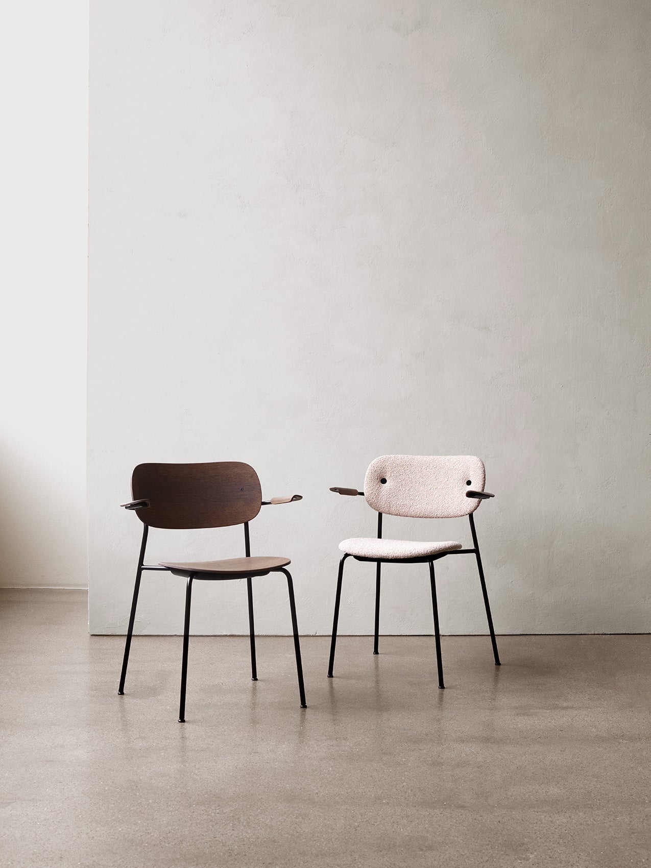 Two versions of the Co Dining Chair with armrests. One in dark stained oak and the other upholstered in a light pink fabric.