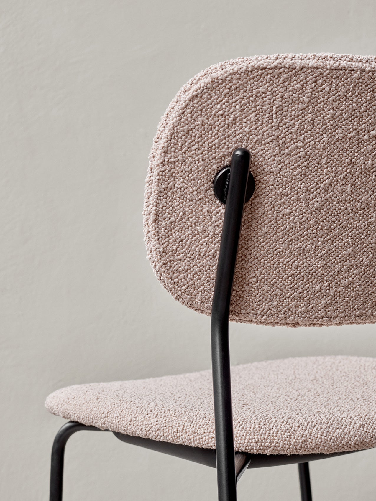A close-up of the back of the Co Dining Chair, featuring textured, light pink bouclé upholstery and black metal frame.